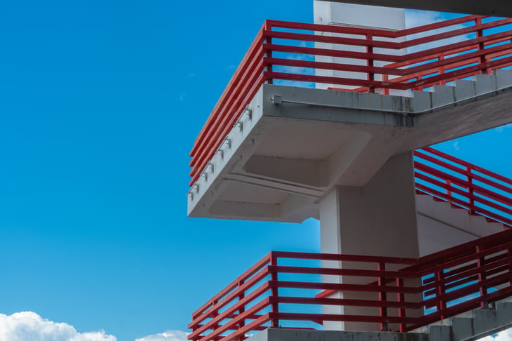 Concrete structure with staircase and red metal railings against blue sky and cloud, pattern or background